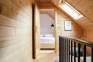 Un interno in legno con soffitto spiovente, un letto con biancheria bianca, una citazione ispiratrice incorniciata e un piccolo cane.