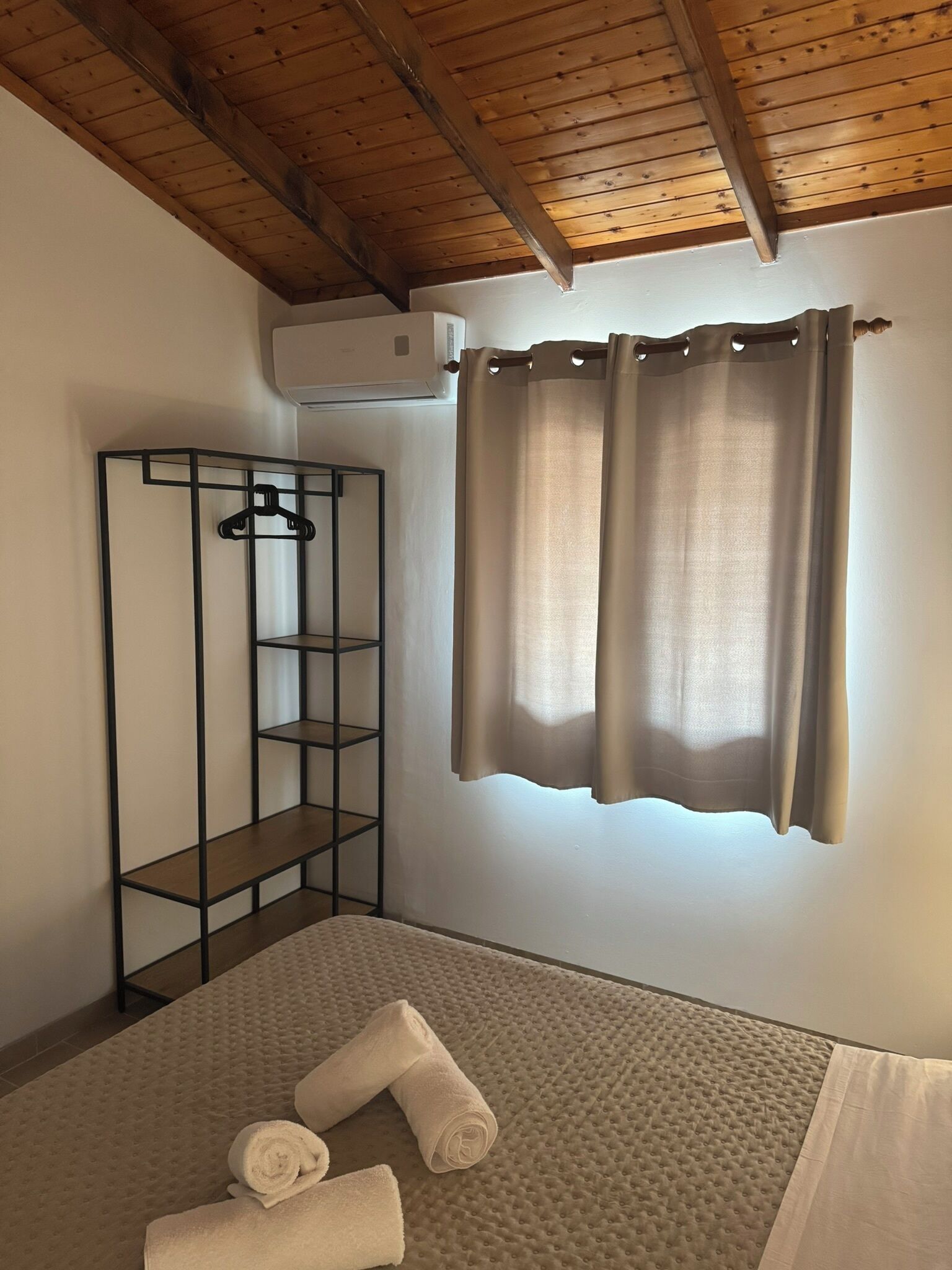 A room with a bed, a hanging wardrobe, and a window with curtains.