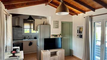 Una cocina moderna con horno integrado, un refrigerador, una mesa de comedor de madera con sillas y un televisor sobre un soporte de madera.