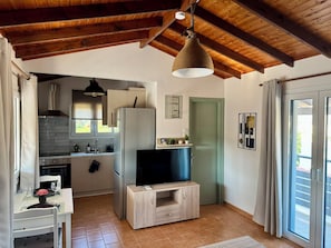 Una cocina moderna con horno integrado, un refrigerador, una mesa de comedor de madera con sillas y un televisor sobre un soporte de madera.