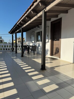 Un patio cubierto con suelo de baldosas, una mesa con sillas y una puerta.