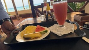 Ein Tablett mit Obst, einem Getränkglas, einem Tisch und Blick auf den Ozean.