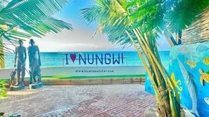 Vista de la playa con un cartel que dice 'I ♥ NUNGWI' y una dirección web.
