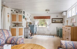 Ein gemütliches Wohnzimmer mit gestreiften Sofas, einem Holztisch, einem Essbereich mit Tisch und Stühlen sowie einer Küchenzeile mit Schränken und einem Kühlschrank.