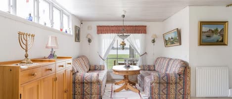 A room with a wooden cabinet, patterned sofa, a round table, and a view of the outdoors.