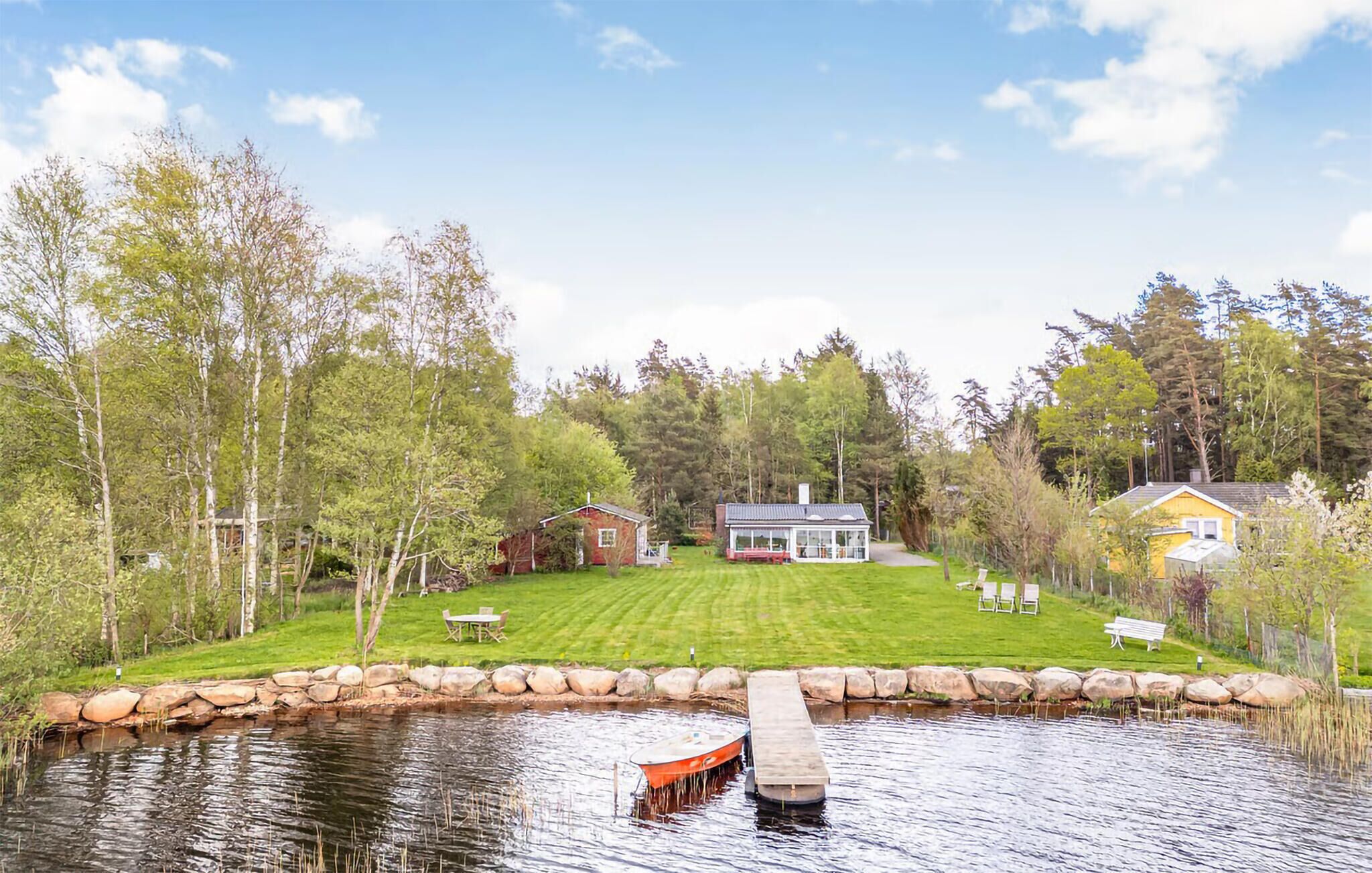 A lakeside property with a dock, a grassy lawn, and a house surrounded by trees.