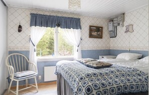 Ein Schlafzimmer mit einem Bett, einem Sessel, einem Fenster mit Vorhängen, einer Heizung und einer an der Wand montierten Elektroinstallation.
