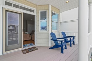 Un porche cubierto con dos sillas Adirondack, una puerta corrediza de vidrio y vistas al interior.