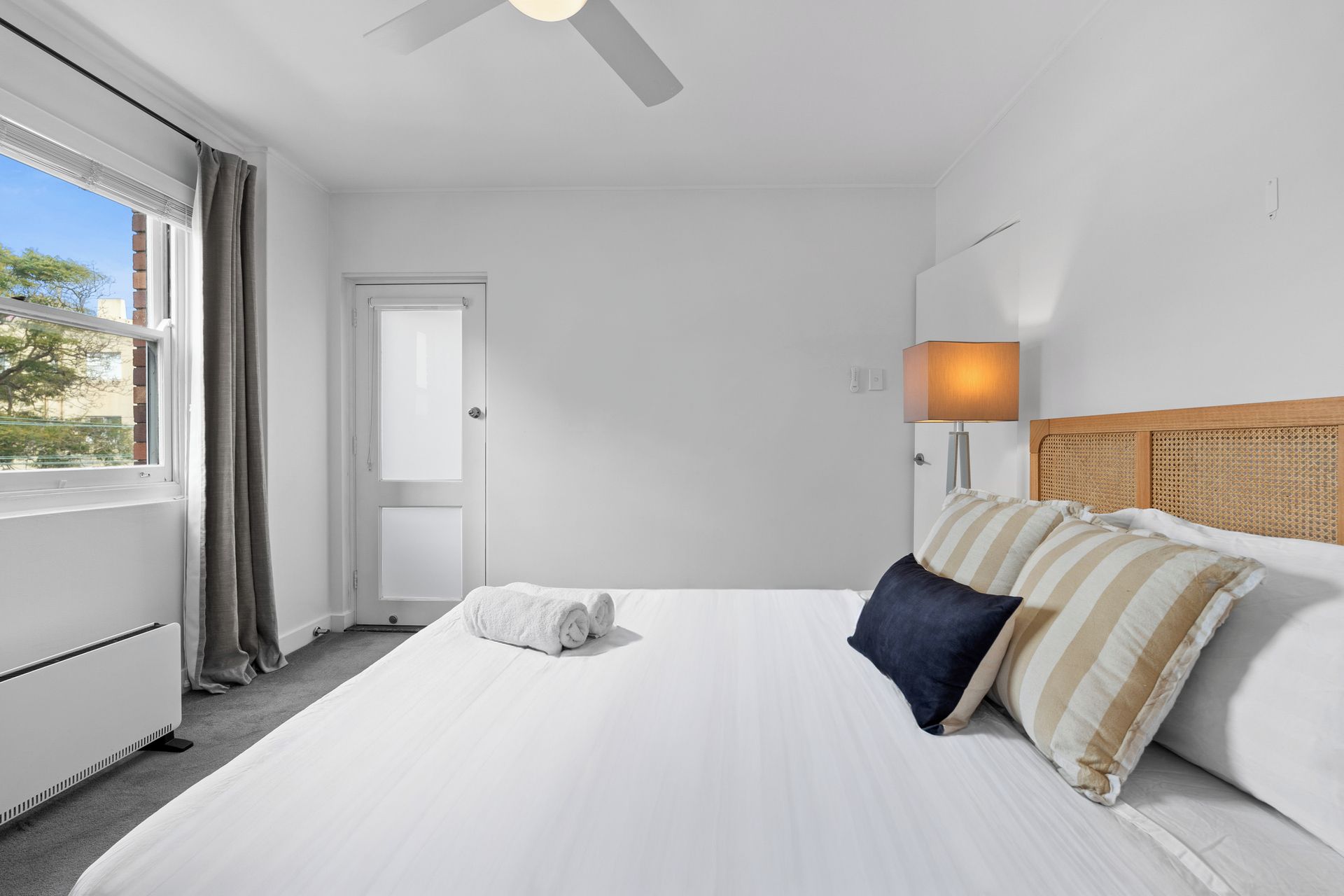 A hotel room with a bed, a bedside lamp, a window with curtains, and a door.