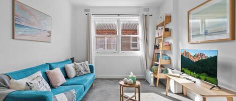 A living room with a teal sofa, a coffee table, a bookshelf, and a TV on a stand.