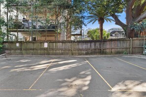 A parking area with marked spaces, a wooden fence, and buildings in the background. - Bright 2BDR Bondi Junction Home with Parking (Bondi Junction)