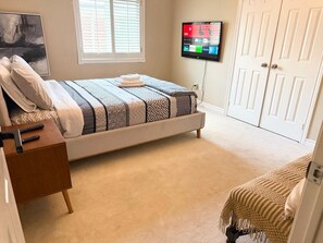 Quarto com cama, televisão, escrivaninha e guarda-roupa.