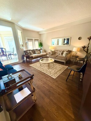 A spacious living room with a large sofa set, a coffee table, and a dining area with a tray table.