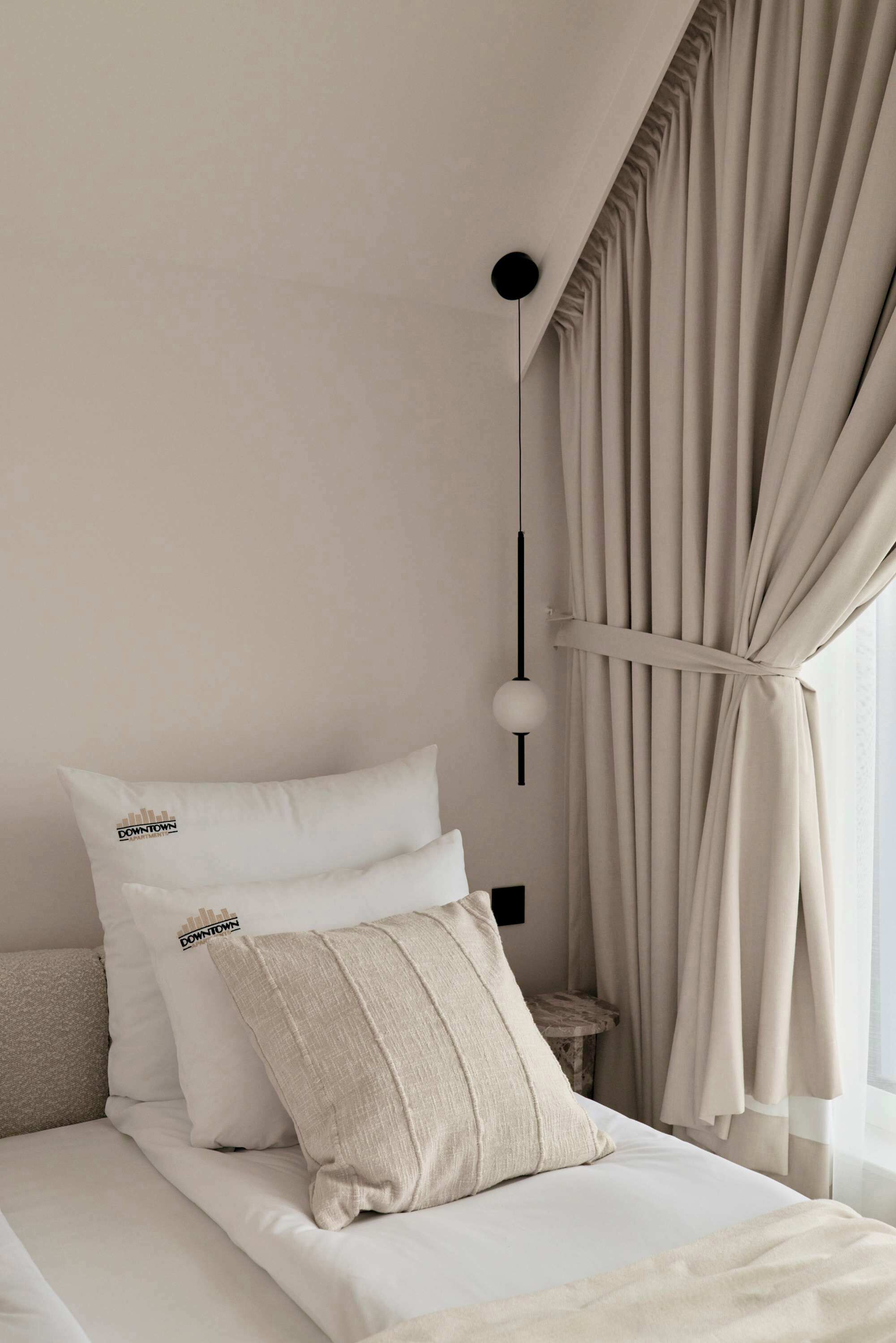 Une chambre à coucher avec un lit, deux oreillers, une table de chevet, une lampe et des rideaux.