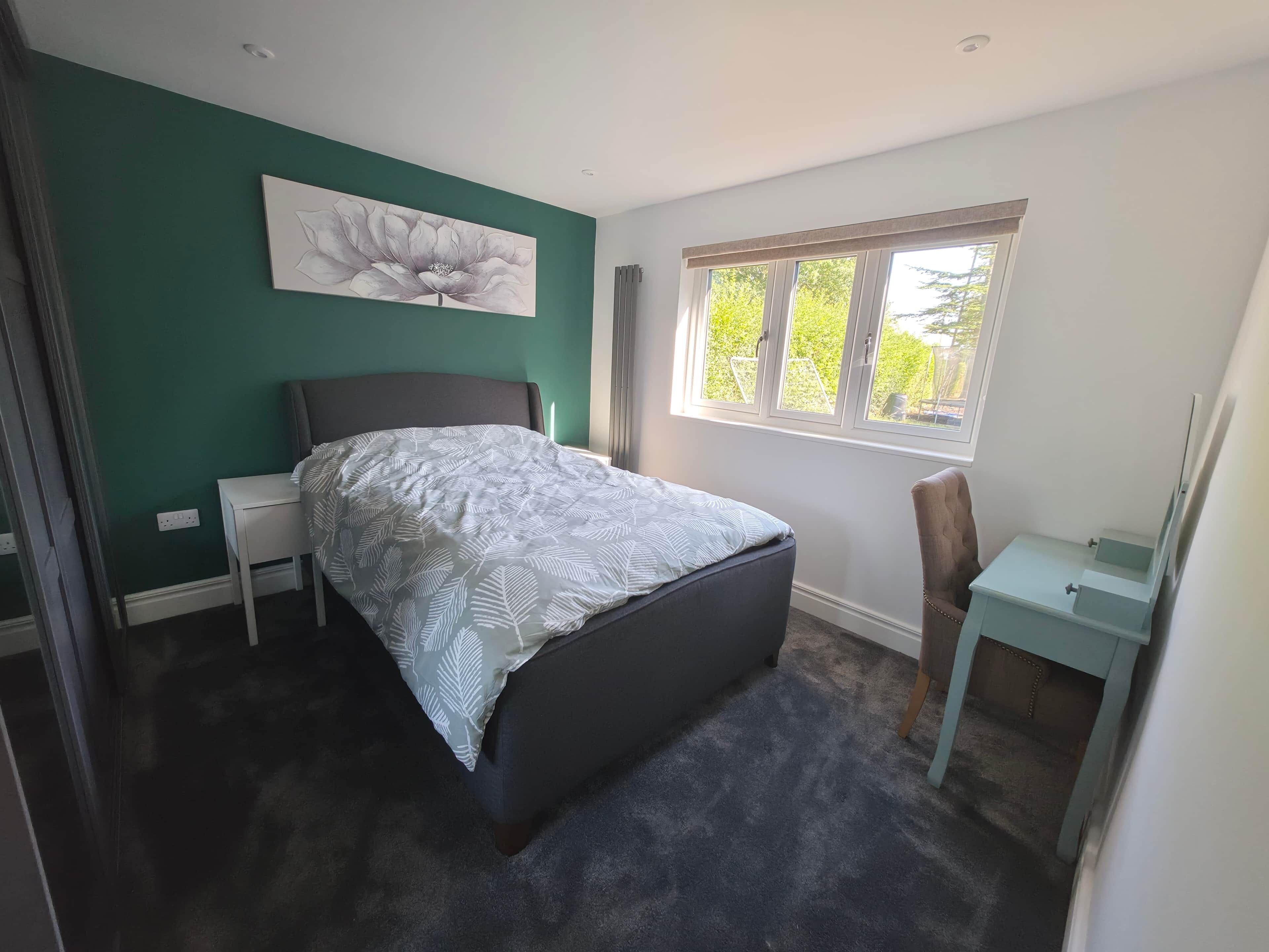 Quarto com cama, mesa de cabeceira, cadeira, janela e um quadro na parede.