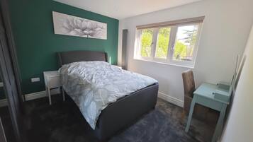 Quarto com cama, mesa de cabeceira, cadeira, janela e um quadro na parede.