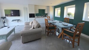 Un salon moderne comprenant un canapé, une table à manger pour quatre personnes et un coin cuisine avec des placards et un téléviseur.