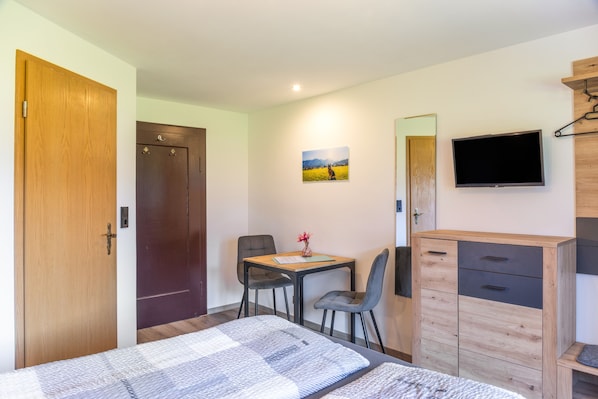 A room with a bed, a desk with a chair, a television, and a wardrobe.