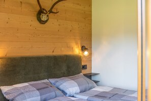 A room with a wooden headboard, a bed with patterned bedding, a wall-mounted light, and a wooden wall with a mounted animal skull. - Room "Zimmer 2 Schulerhof" with Mountain View and Wi-Fi (Oberau)