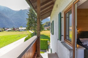 Un balcon donnant sur un paysage montagneux, avec une balustrade en bois et une porte menant à une pièce où se trouve un lit.