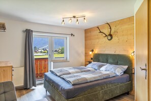 Un dormitorio con una cama, un ventanal con vistas al exterior, una pared de madera y una cabeza de animal montada.