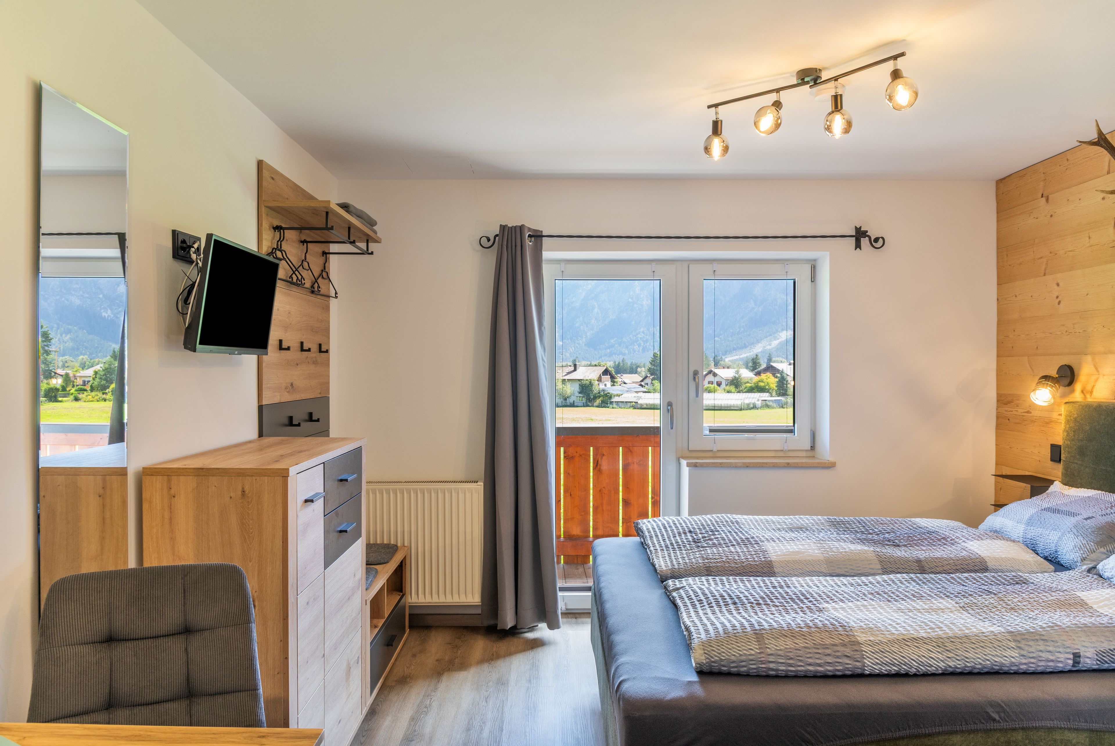 Ein Schlafzimmer mit Bett, Schreibtisch, Stuhl, Fernseher und einem Fenster mit Blick auf Berge.