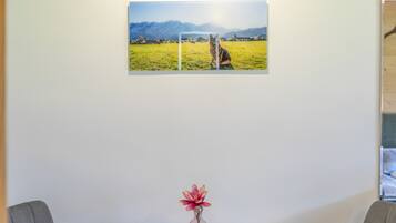 Ett inramat fotografi som föreställer ett fält med berg i bakgrunden, en vas med blommor på ett bord och två stolar.