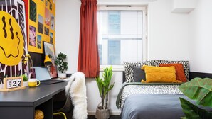 A modern bedroom with a desk, a bed with patterned bedding, a window with blinds, and a wall decorated with various pictures. - Student Only Cross Court House (London)