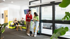 A reception area with a glass door, a flat-screen TV, and a seating area with a green couch and a small table. - Student Only Cross Court House (London)