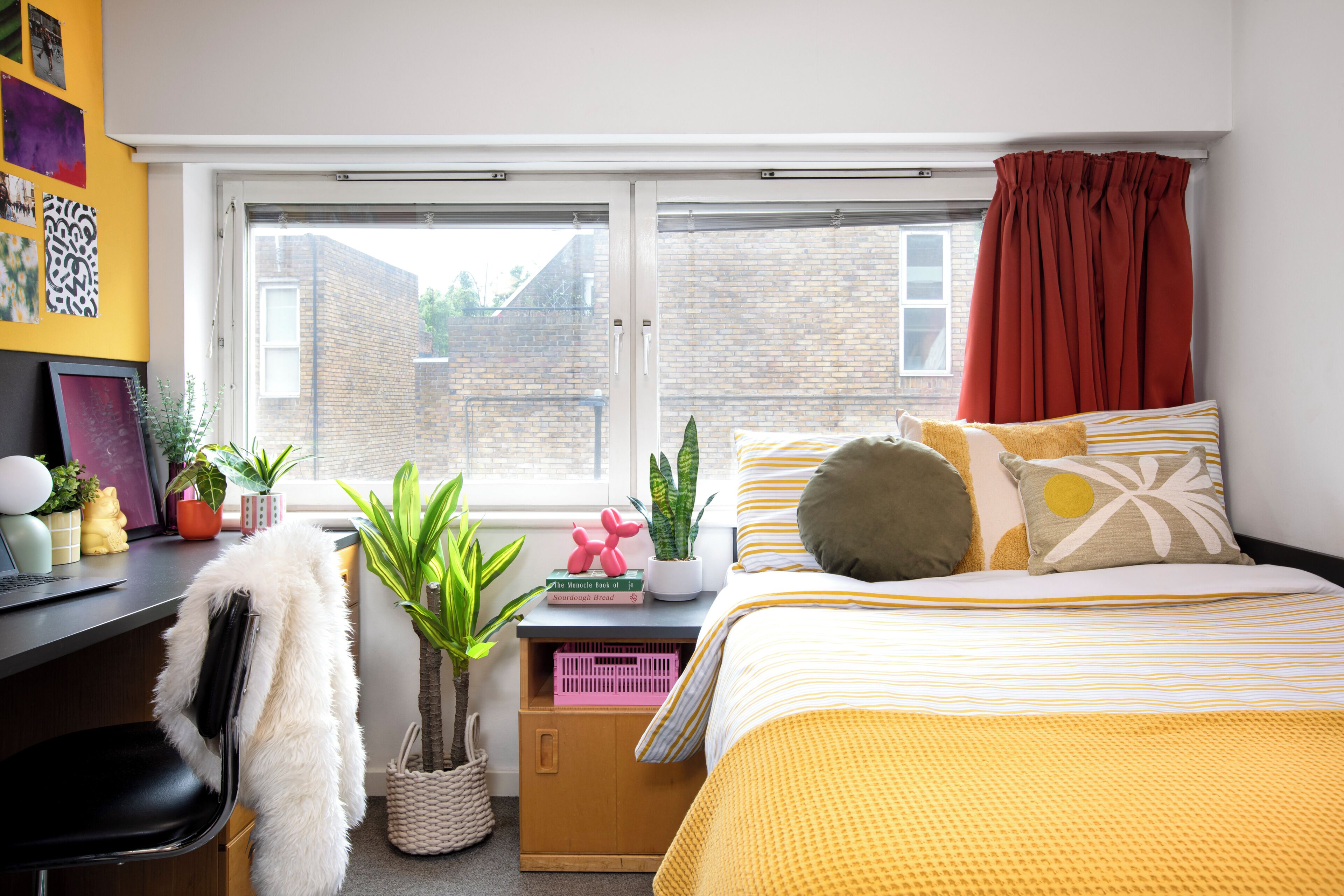 Une chambre à coucher avec un lit, un bureau, une fenêtre et diverses plantes.