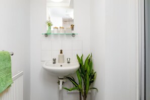 A bathroom with a white sink, a mirror above it, and a green plant beside the sink. - Student Only Cross Court House (London)