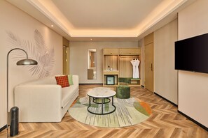 A modern hotel room with a sofa, a round coffee table, a TV, and a wardrobe.