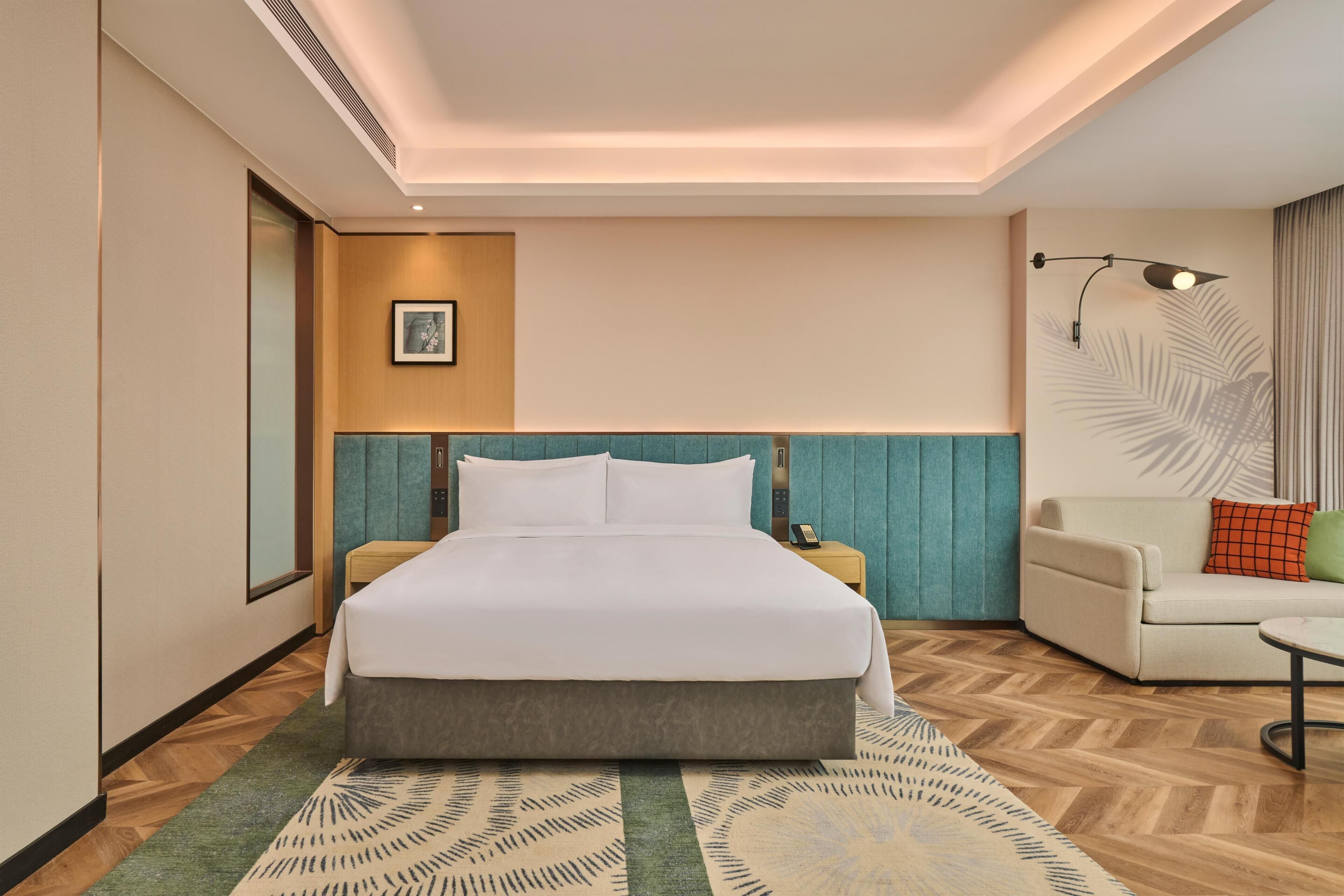 A hotel room with a large bed, a bedside table with a phone, a chair, and a decorative wall panel.