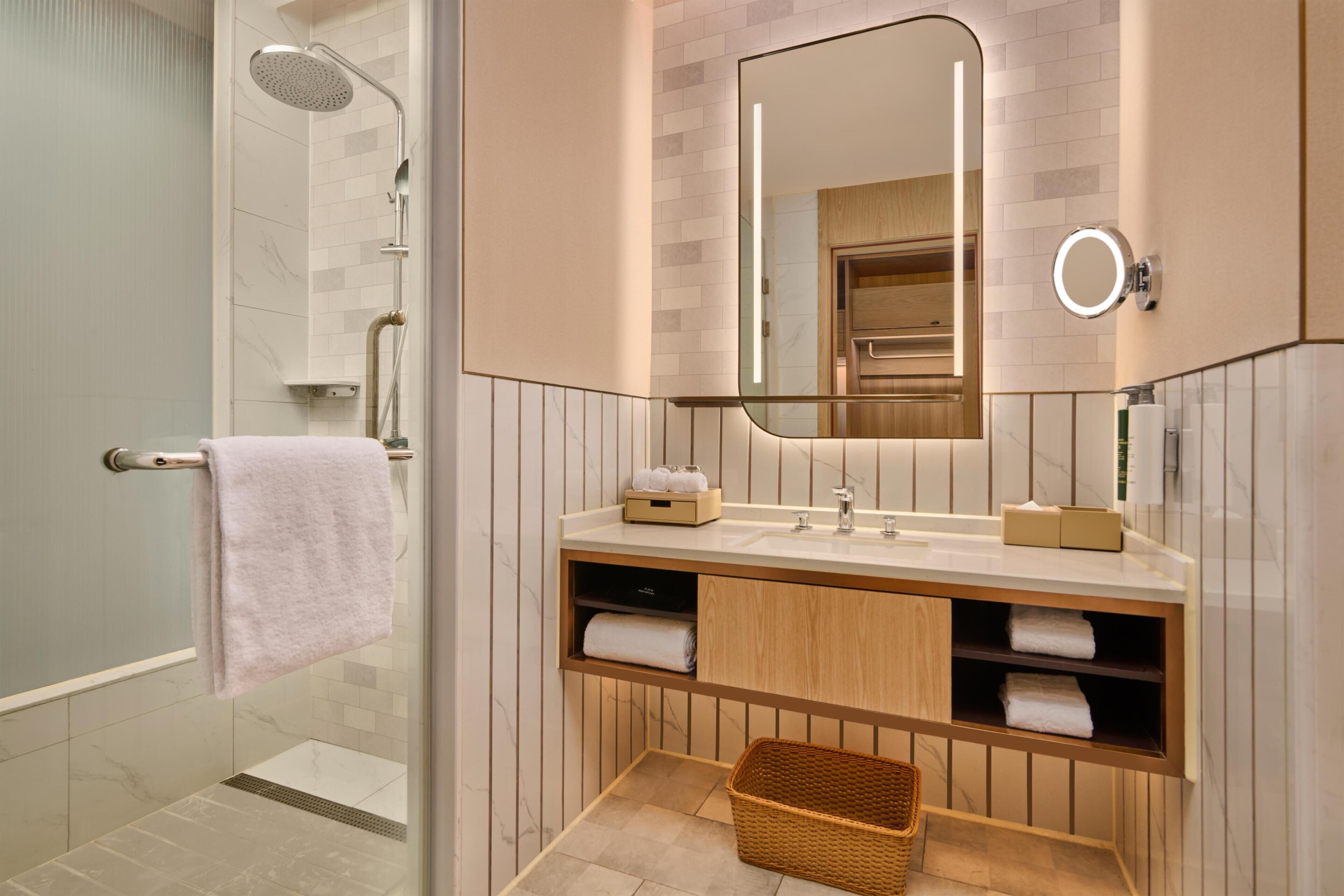 A modern bathroom with a glass-enclosed shower, a vanity with a mirror, and a wicker basket.