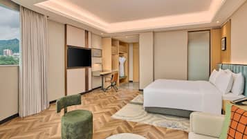A hotel room with a bed, a desk, a chair, a television, and a view of the city.