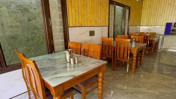 A dining area with wooden tables and chairs, a marble floor, and a view through a glass door. - Hotel Ekant Valley (Chakrata)