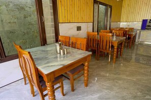 Un comedor con mesas y sillas de madera, piso de mármol y vista a través de un ventanal.