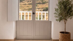A room with a door leading to a balcony with a view of a hilly landscape. - Dryope Luxury Living (Kithnos)