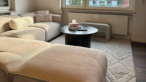 A living room with a sectional sofa, a round coffee table, and a large window with a view of houses and trees. - View of Karlstadt Castle (Karlstadt)