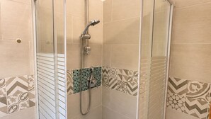 A glass-enclosed shower stall with a handheld showerhead, tiled walls with geometric patterns, and a corner door. - Casa Vacanze San Teodoro (San Teodoro)