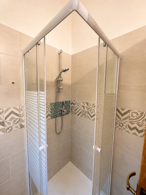 A glass-enclosed shower stall with a handheld showerhead, tiled walls with geometric patterns, and a corner door. - Casa Vacanze San Teodoro (San Teodoro)