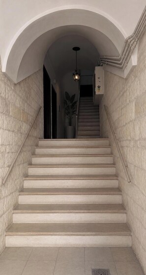 A staircase with a stone wall on either side, leading to a landing with a light fixture.