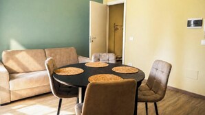 A room with a round table, four chairs, a sofa, and a door leading to another room. - San Francesco Residence (Trani)