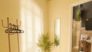 A hotel room with a wooden floor, a coat rack, a potted plant, a mirror, and a bathroom visible through an open door. - San Francesco Residence (Trani)