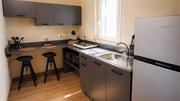 A compact kitchen with a refrigerator, a sink, and two stools. - San Francesco Residence (Trani)