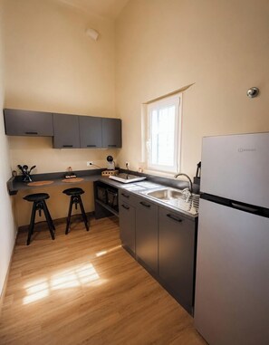 A compact kitchen with a refrigerator, a sink, and two stools.
