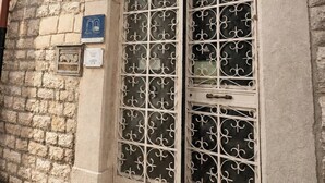 A building with a stone facade, a large arched window with decorative metal grilles, and a blue sign indicating a port train. - San Francesco Residence (Trani)