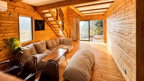 A cozy cabin interior with a lofted sleeping area, a dining table, and a sofa. - Log Cabin with Ocean Views | Bonfire in a Private Satoyama Forest (富津市)