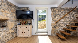 A room with stone walls, a wooden floor, a TV mounted on the wall, a cabinet with drawers, and a wooden staircase. - Villa Jura by Villas Guide (Bribir)