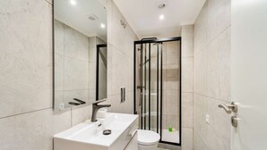 Et moderne badeværelse med en hvid vask, toilet og et bruseområde med glasvægge.